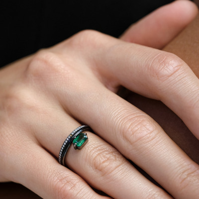 Close-up of a hand wearing a ring featuring an emerald and diamond accents.