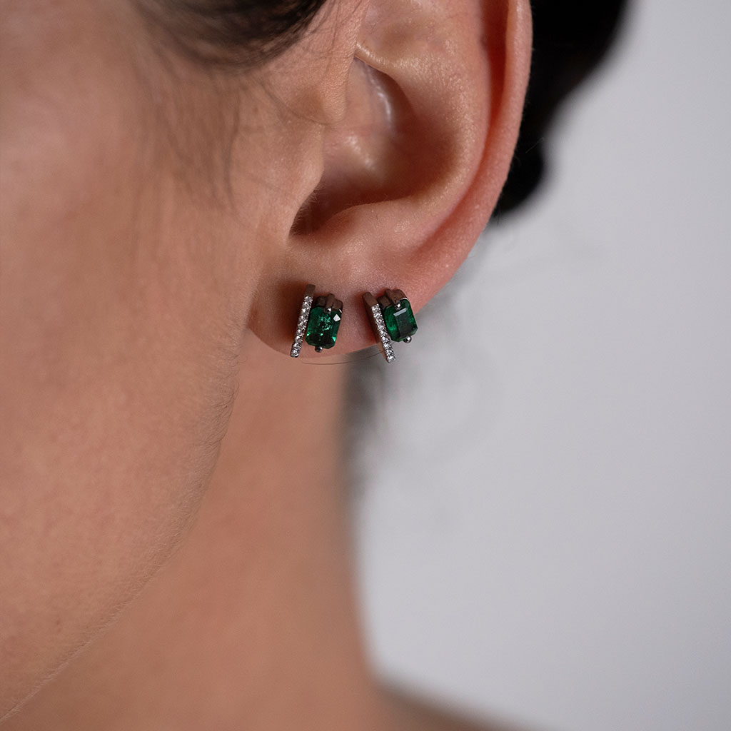 Emerald stud earrings featuring diamond accents, showcasing a close-up of the jewelry worn on the ear.