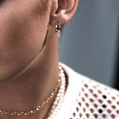 Close-up of a gold hoop earring with diamond accents worn by a model, showcasing elegant jewelry design.
