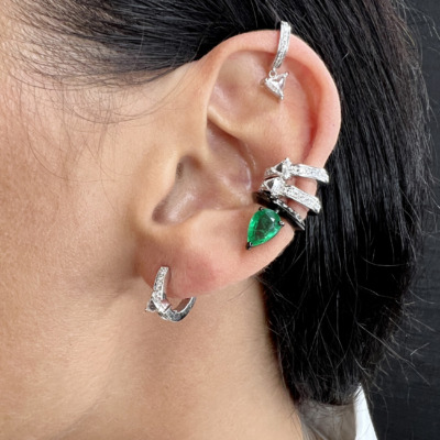 Close-up of an ear adorned with multiple silver rings and an emerald earring.