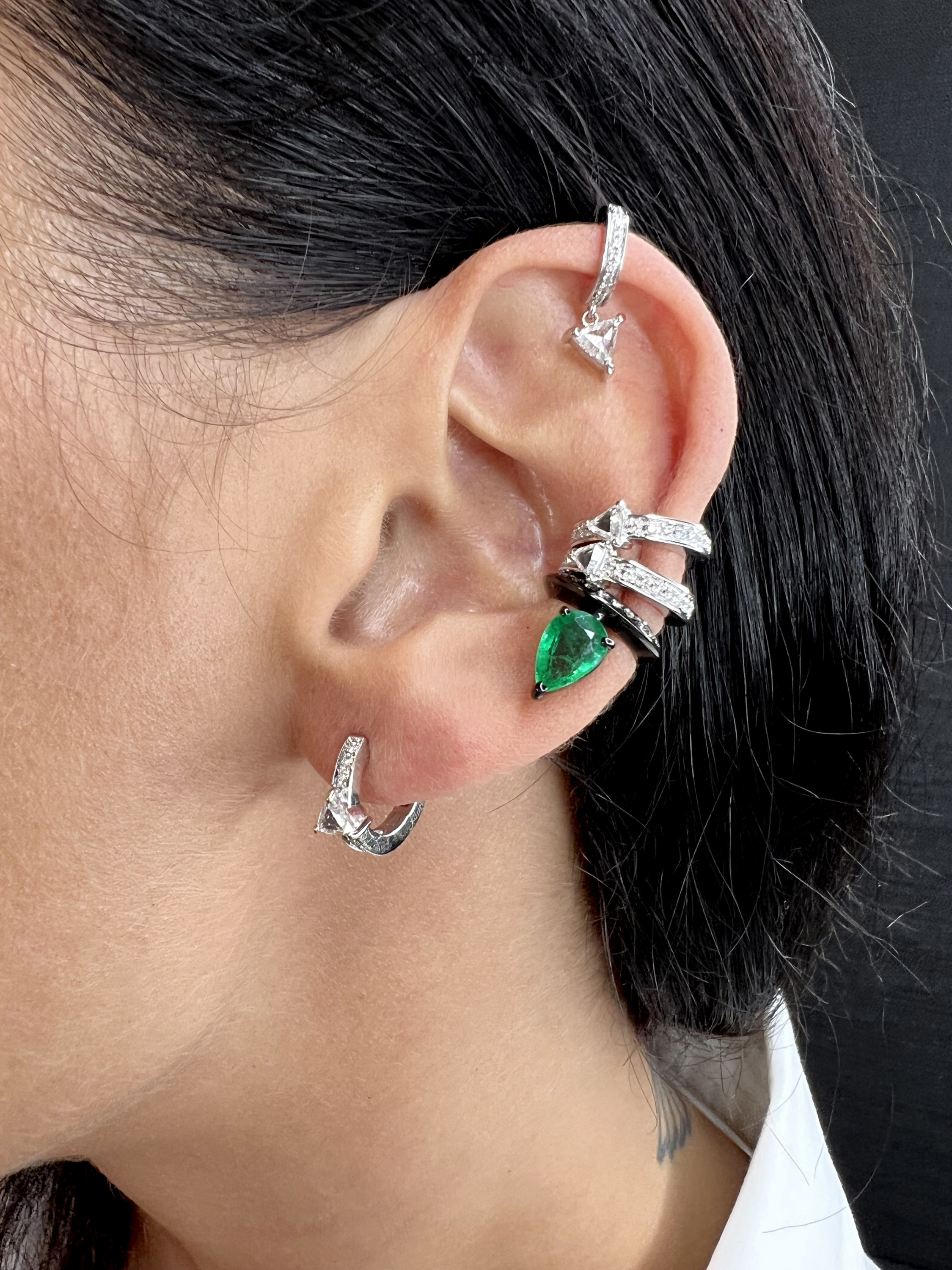 Close-up of an ear adorned with multiple silver rings and an emerald earring.