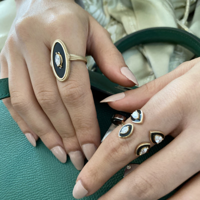 Close-up of a hand wearing multiple rings, including an oval black ring and a green handbag in the background.