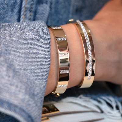 Three bangle bracelets in gold and silver worn on a wrist, featuring a mix of smooth and textured designs.