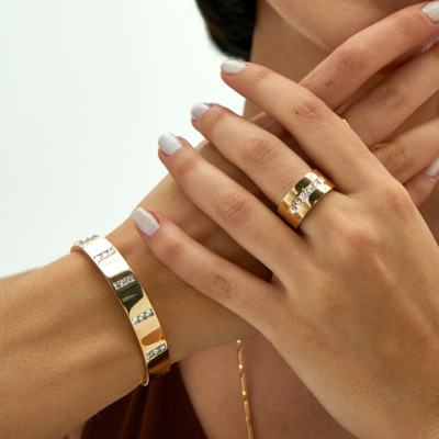 Gold bracelet and ring with diamond-like accents worn on a person's hands.