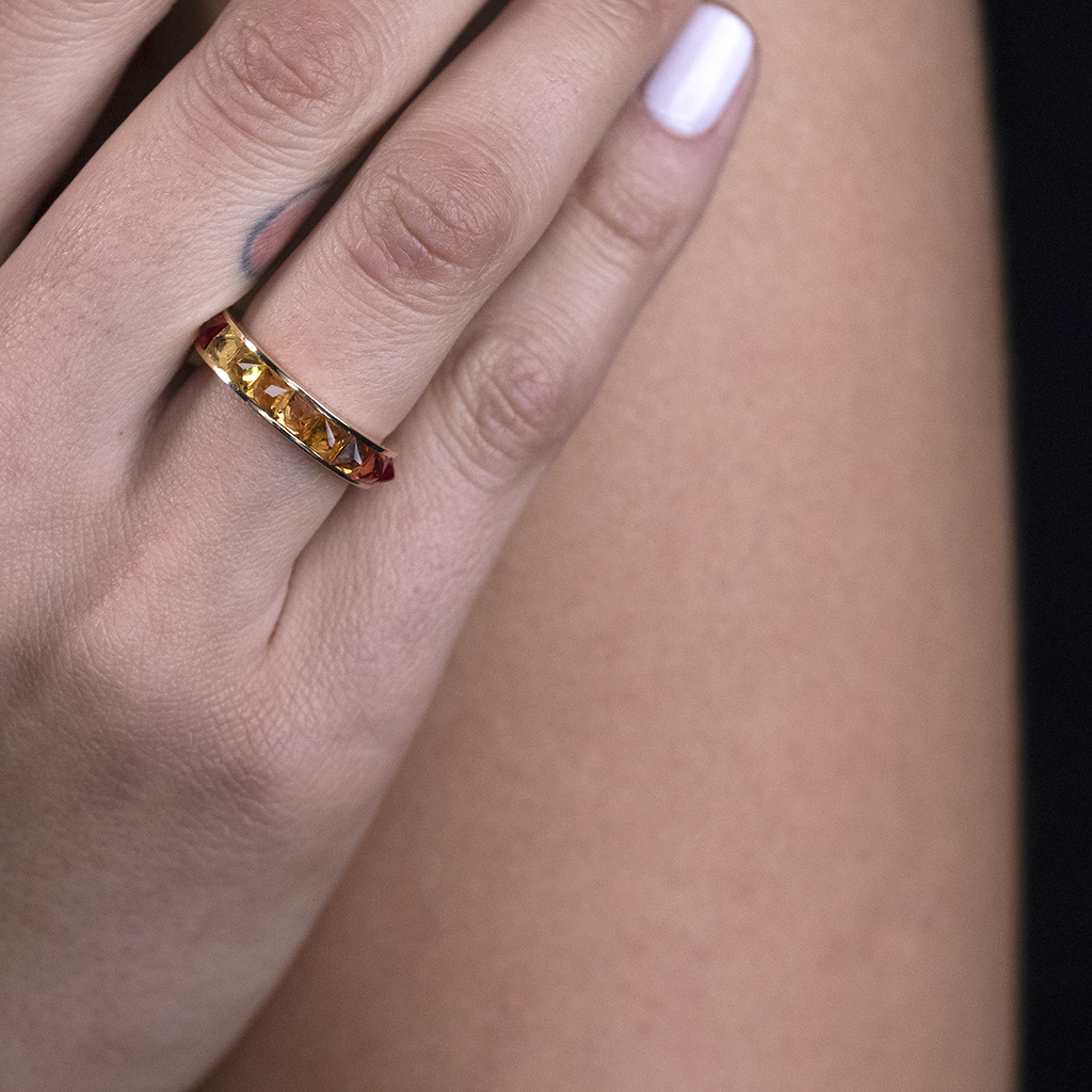 Close-up of a hand wearing a gold ring adorned with red gemstones.