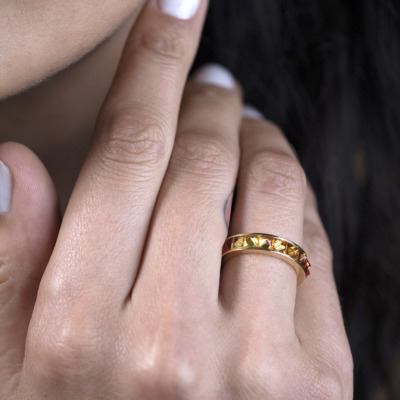 Close-up of a hand wearing a gold ring with colored stones on the finger.