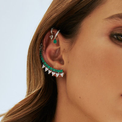 Close-up of a woman's ear adorned with silver and green statement earrings featuring geometric designs.