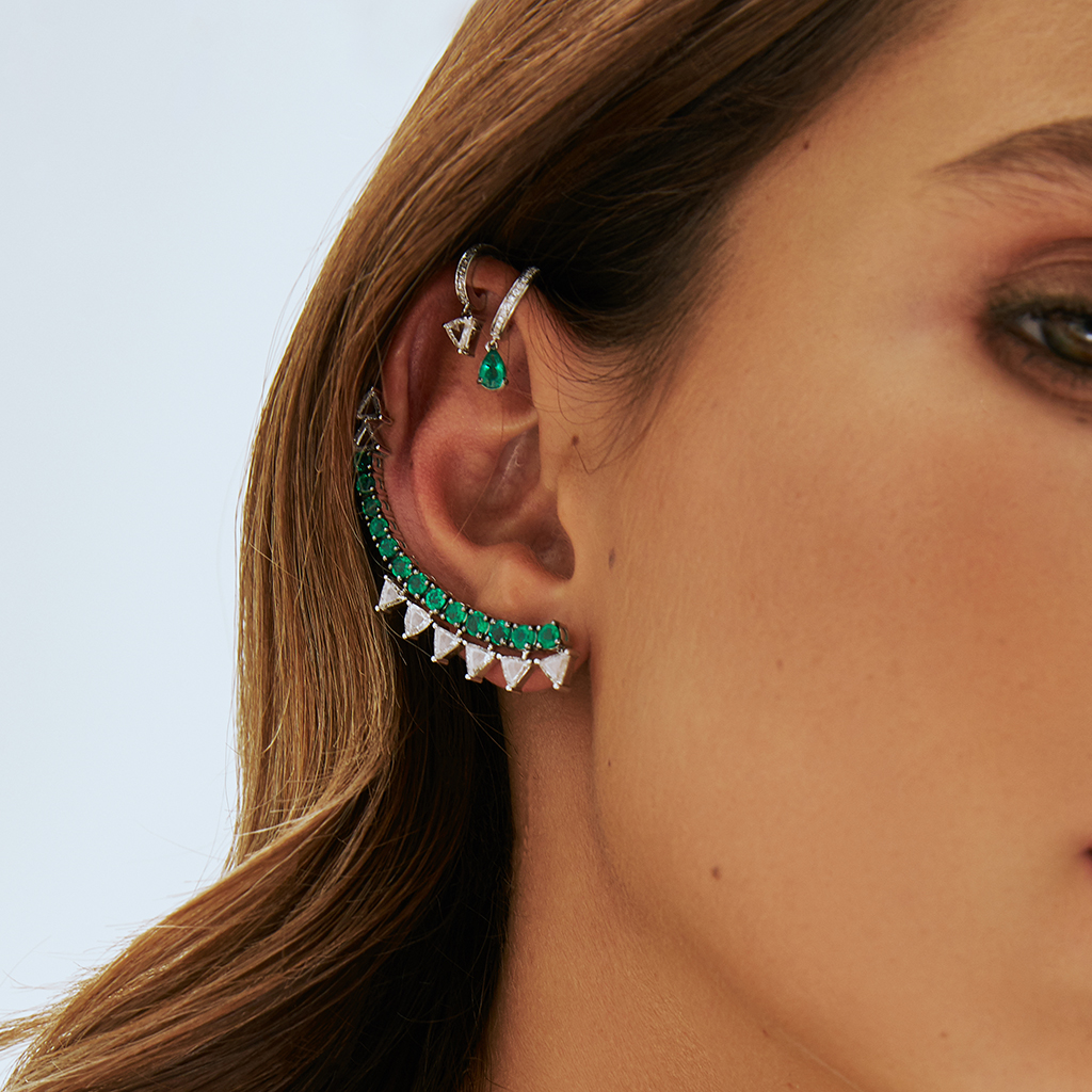 Close-up of a woman's ear adorned with silver and green statement earrings featuring geometric designs.