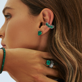 Profile view of a woman with earrings and rings featuring emerald stones.