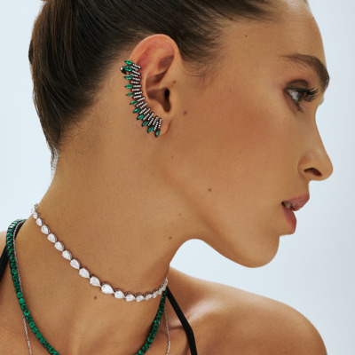 Profile view of a model showcasing earrings and necklaces with green and silver elements.