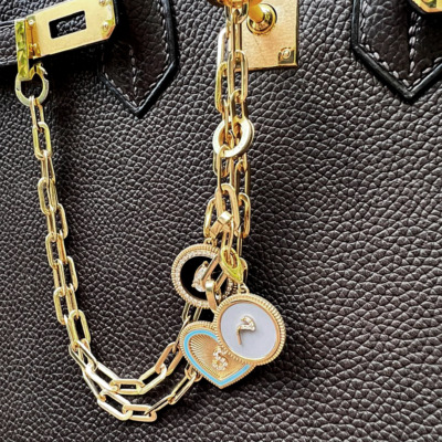 Gold chain featuring heart and circular charms attached to a black textured handbag.