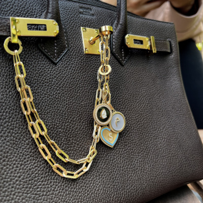 Black leather handbag featuring a gold chain and decorative charms attached to the handle.