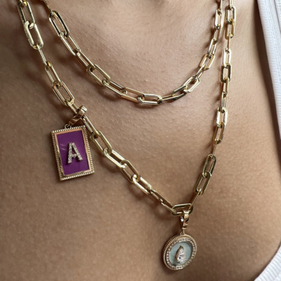 Close-up of layered gold necklaces featuring a purple pendant with an 'A' and a circular pendant with a diamond accent.