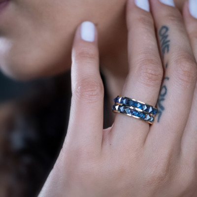 Close-up of a model's hand wearing a silver and black studded ring with a tattoo visible on the finger.