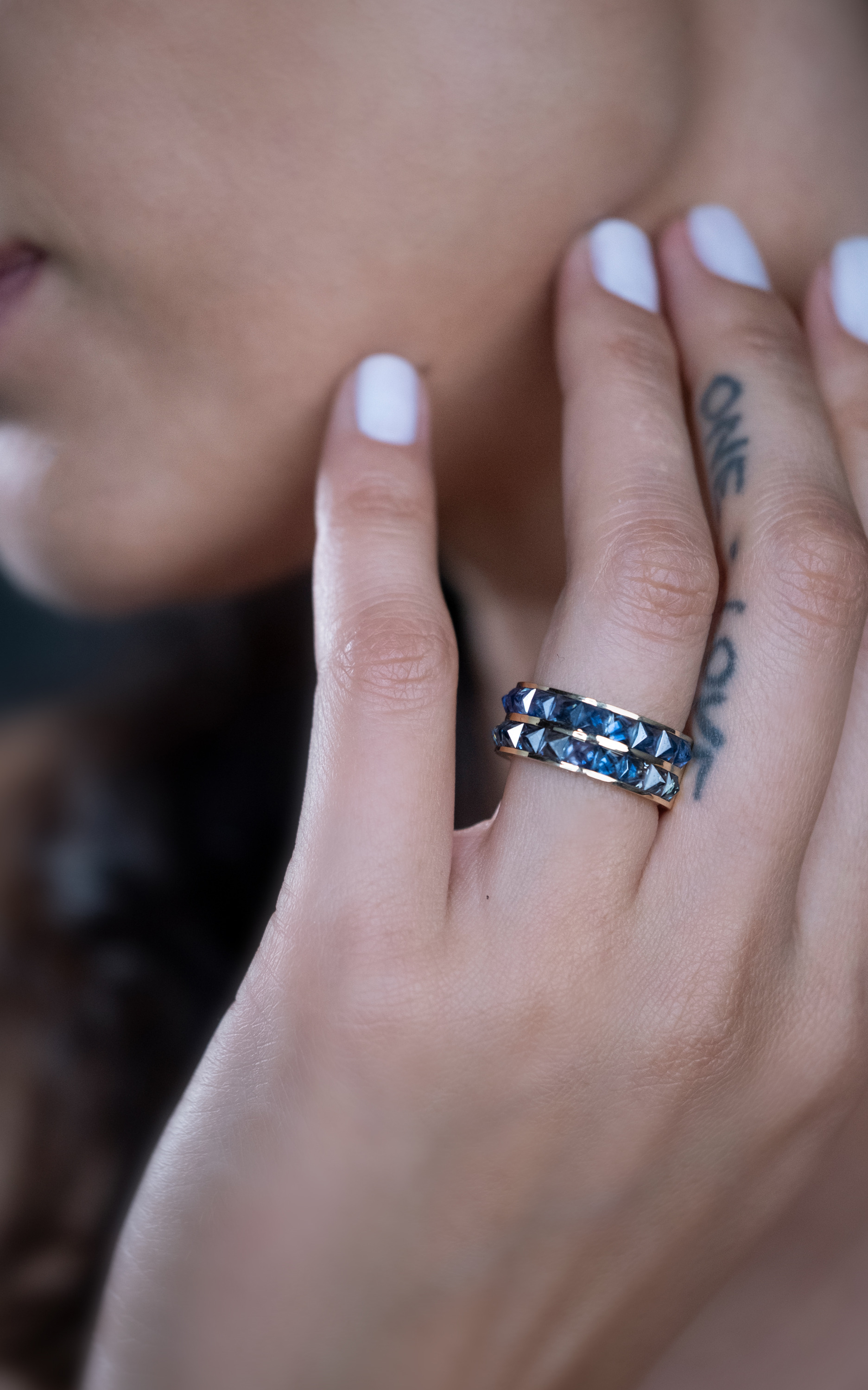 Close-up of a model's hand wearing a silver and black studded ring with a tattoo visible on the finger.
