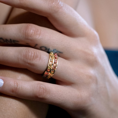 A close-up of a hand wearing a gold and silver ring adorned with colored stones.
