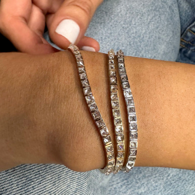 Three silver bracelets with clear stones worn on a wrist against a denim background.