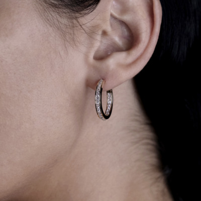 Close-up of a person's ear wearing gold hoop earrings with clear stones.