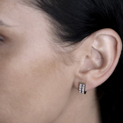 Close-up of a person's ear wearing silver earrings with clear stones.