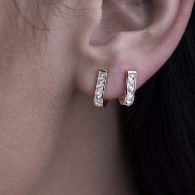 Close-up of gold hoop earrings featuring clear stones, worn on a person's ear.