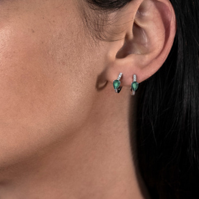 Close-up of a woman's ear wearing emerald and diamond earrings.
