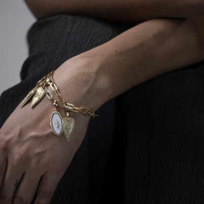Gold charm bracelet featuring heart and shield pendants worn on a wrist.