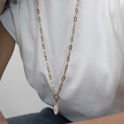 Gold chain necklace featuring an oval pendant worn by a person in a white shirt.