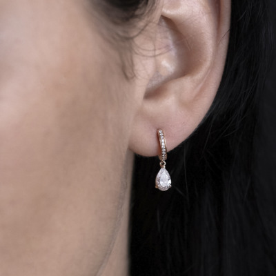Close-up of a woman's ear wearing gold drop earrings with a pear-shaped diamond and small accent diamonds.