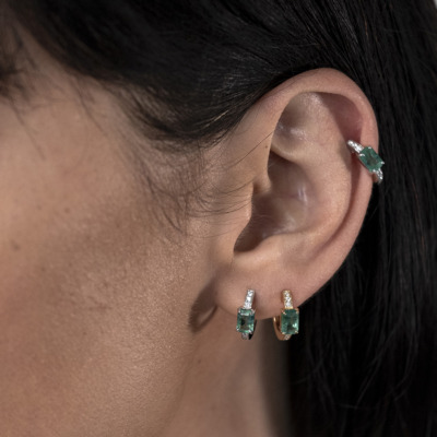 Close-up of a woman's ear adorned with emerald and diamond earrings.