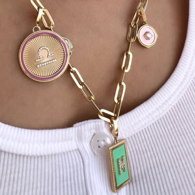 Gold chain necklace featuring multiple charms, including a round charm with a portrait and a rectangular charm with a letter.