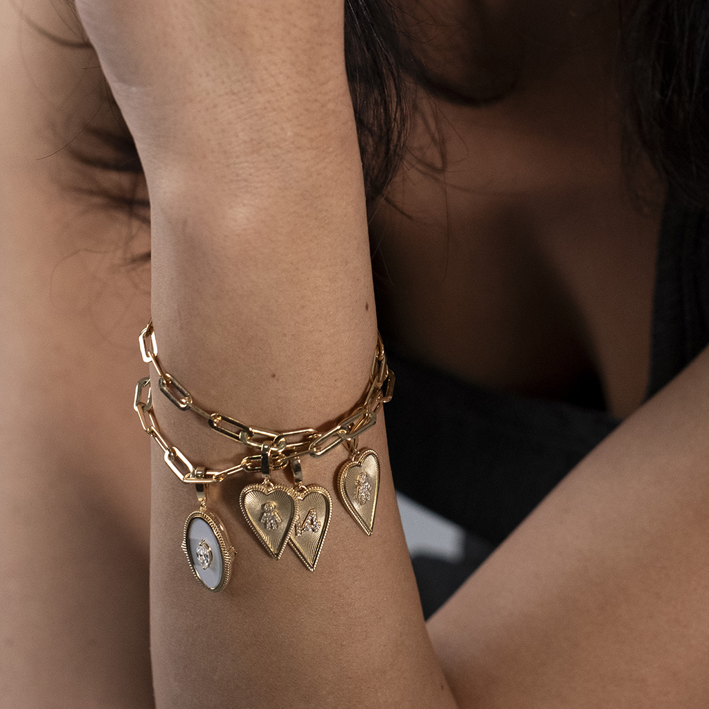 Gold bracelet featuring multiple heart-shaped charms and a decorative oval charm on a wrist.