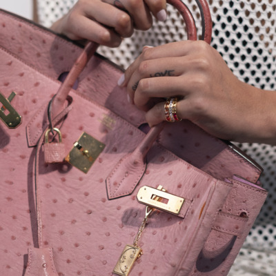 Close-up of a pink ostrich leather handbag held by a person with a ring on their finger.