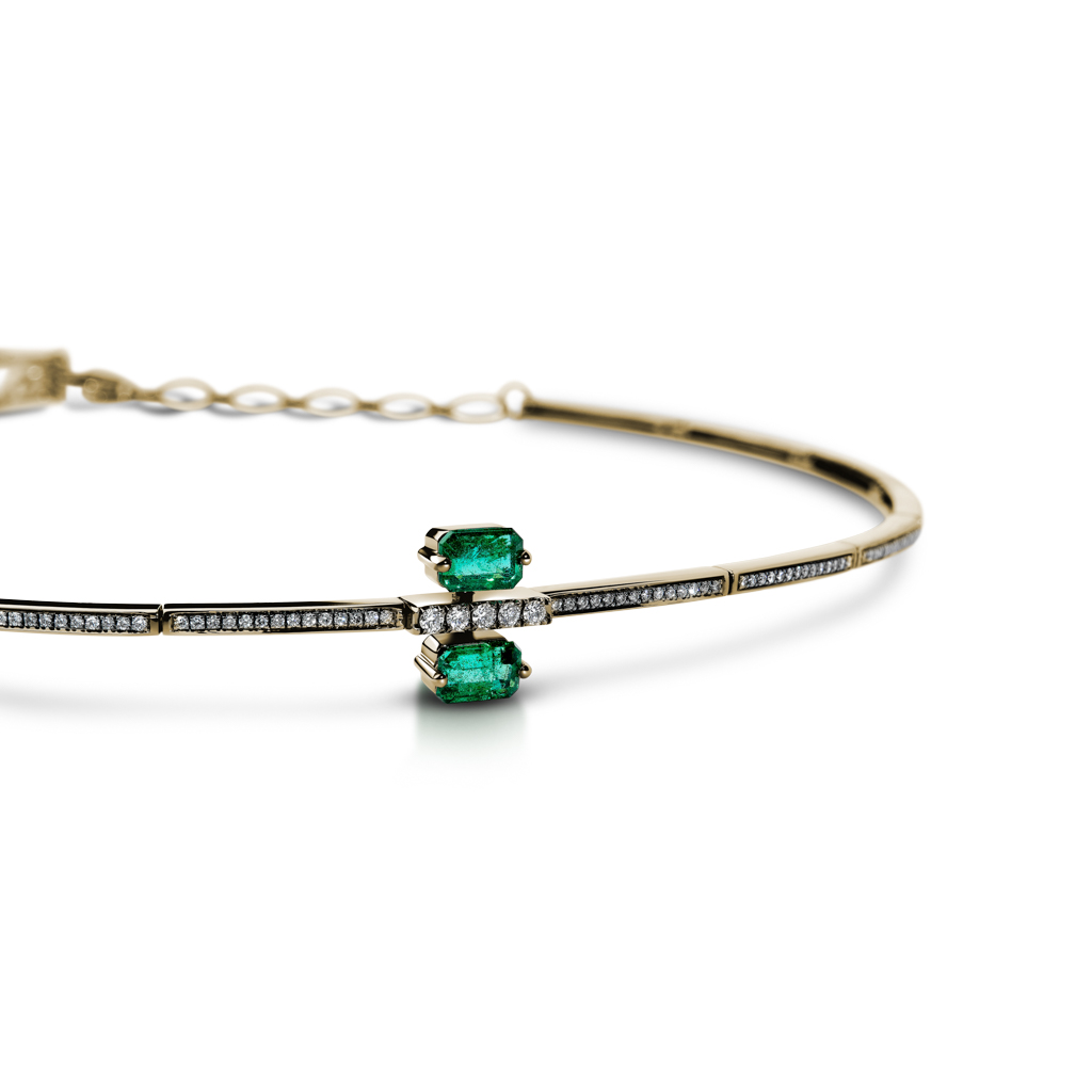 Gold choker featuring two emerald stones and diamond accents on a thin band.