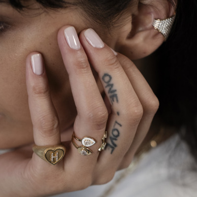 Close-up image of a hand adorned with multiple rings and a single earring, featuring a tattoo on the finger.