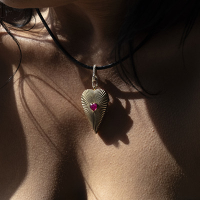 Gold heart-shaped pendant with a pink gemstone on a black cord worn around the neck.