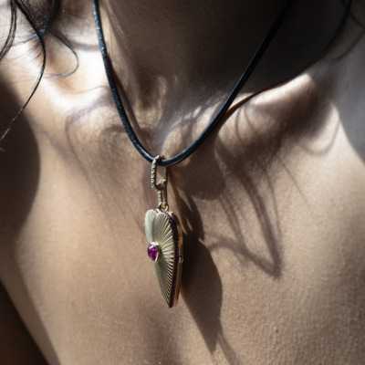 Gold pendant necklace featuring a shell design with a ruby gemstone, worn on a person's neck.