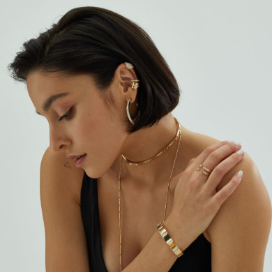 A woman with short hair wearing multiple pieces of gold jewelry including earrings, a choker, and bracelets.