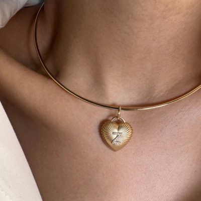 Gold puffy heart charm pendant hanging from a thin gold choker necklace worn on a person's neck.