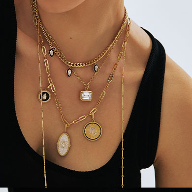 Collection of layered gold necklaces featuring various pendants and charms on a model's neck.