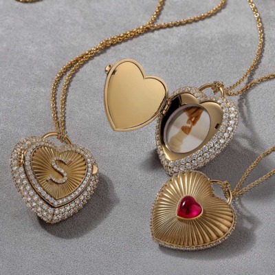 Three gold heart-shaped lockets, two adorned with diamonds and one with a red gemstone, displayed on a textured surface.