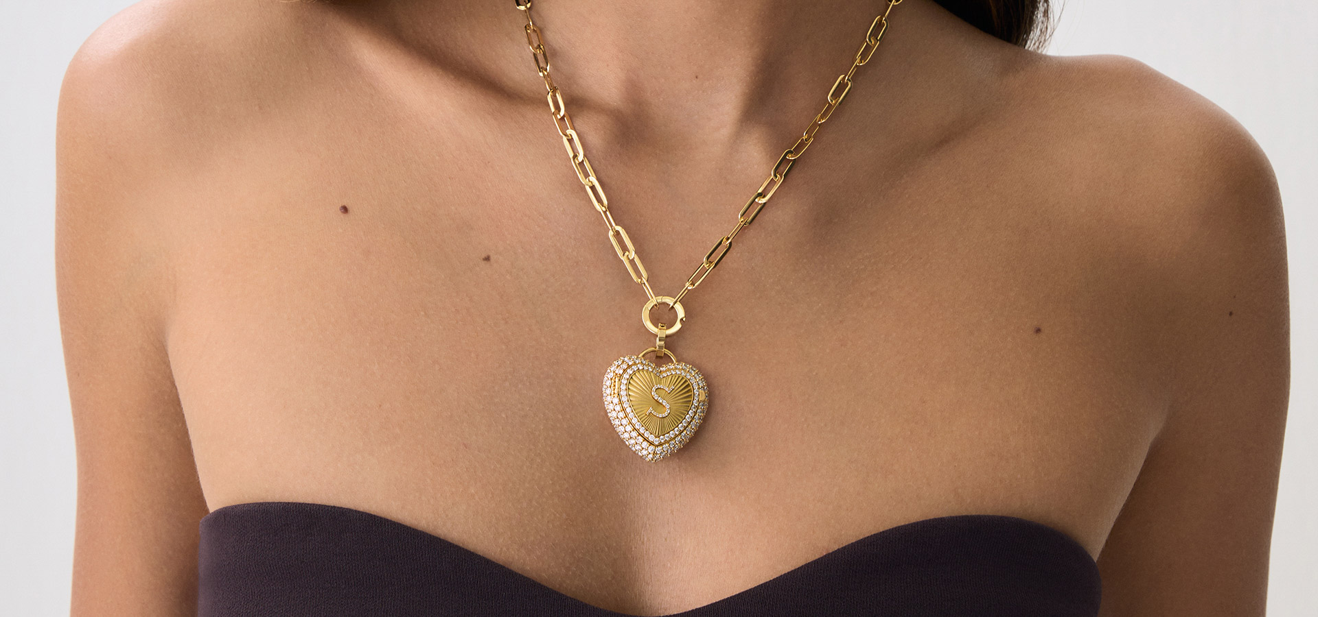 Savolinna gold heart-shaped pendant necklace with a diamond-encrusted rim and chunky links, on a model’s bare chest