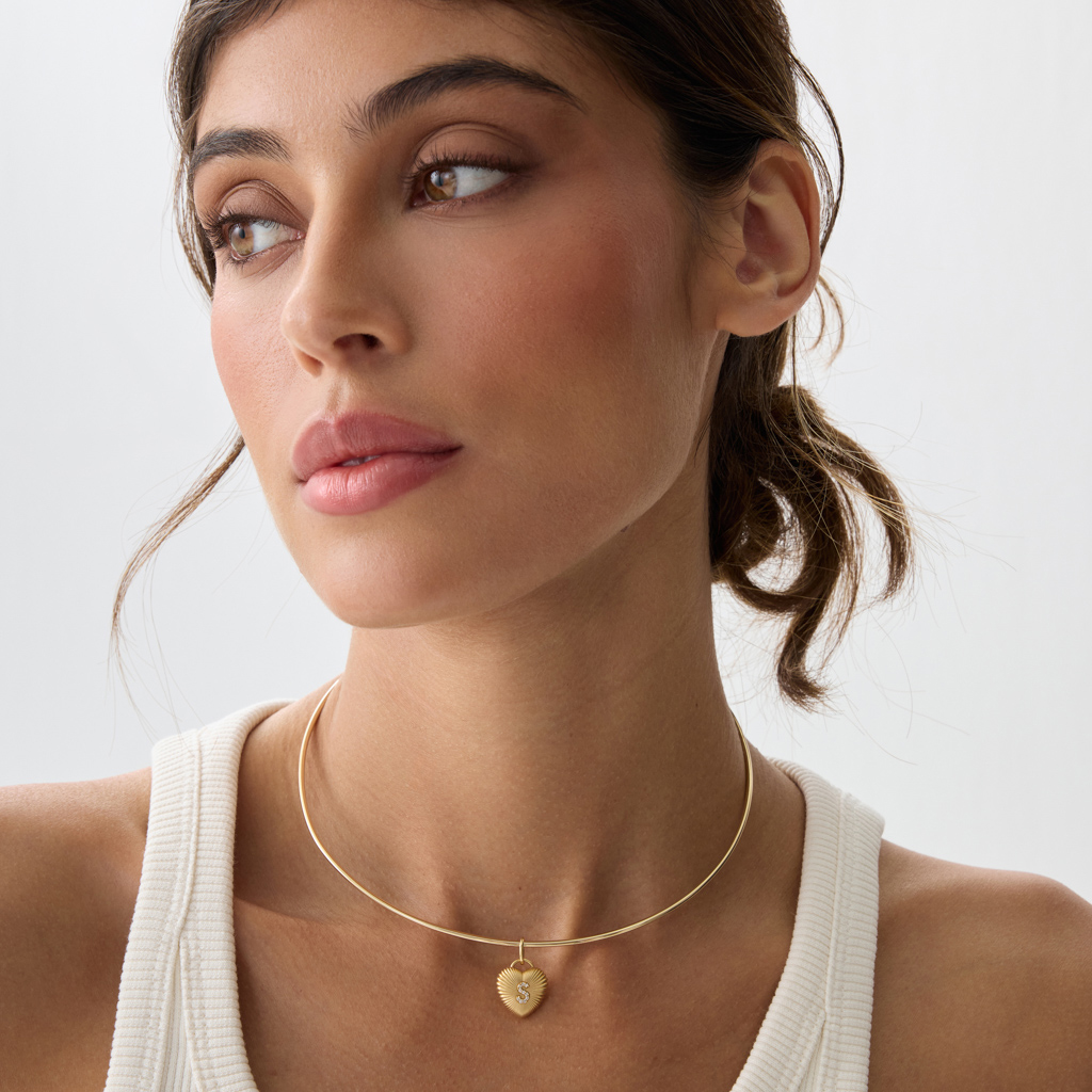 Savolinna gold choker necklace with a small heart pendant featuring a textured heart detail, worn by a model with soft makeup and neutral tones